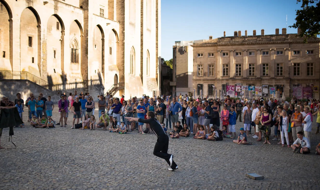 Devant le Palais des Papes, la foule apprécie un artiste qui se donne en spectacle en parallèle avec le festival  © iStock / HaizhanZheng